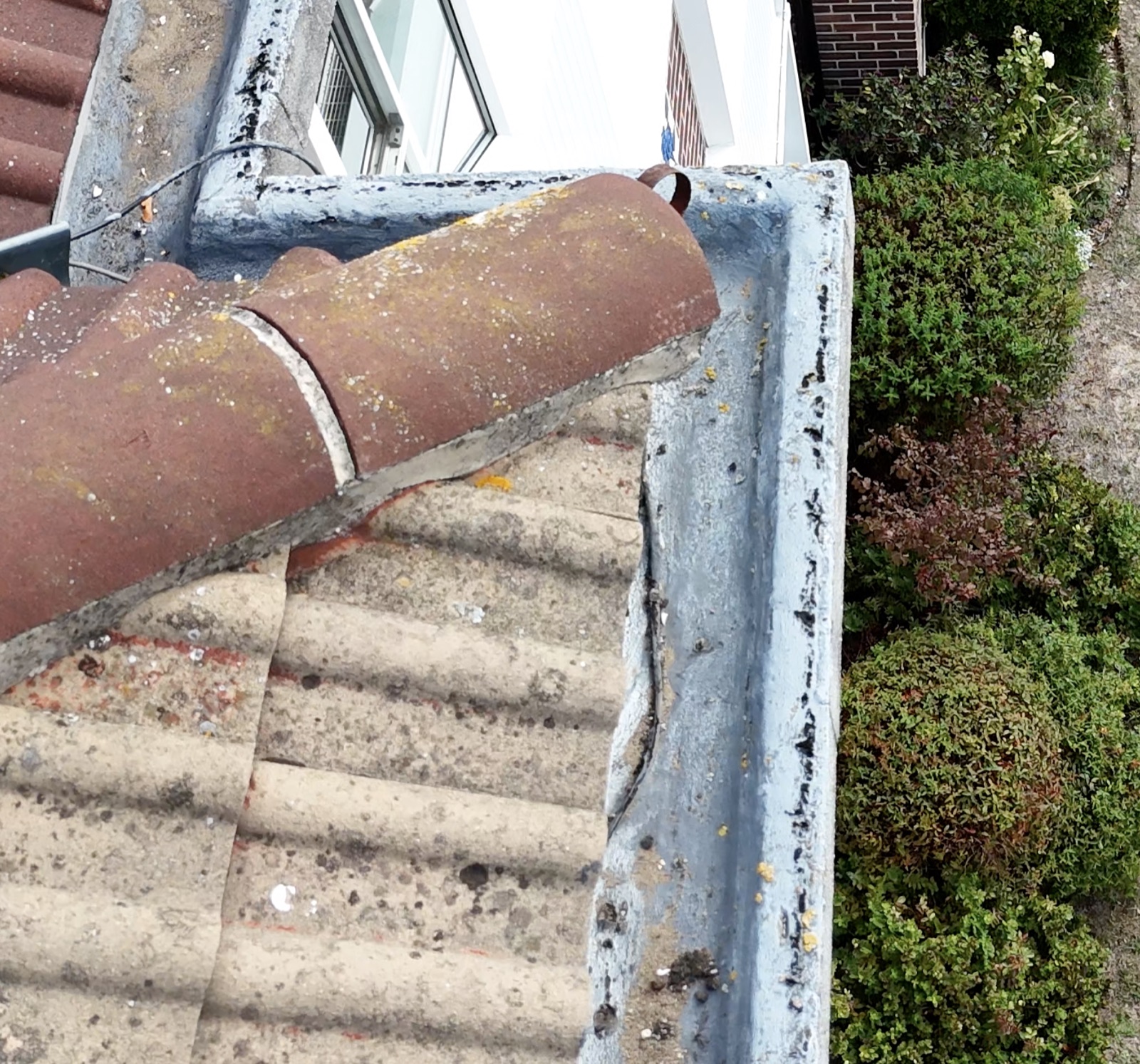 Overhead view of a precast concrete eaves gutter trough with a pale asphalt lining, meeting a pitched roof.