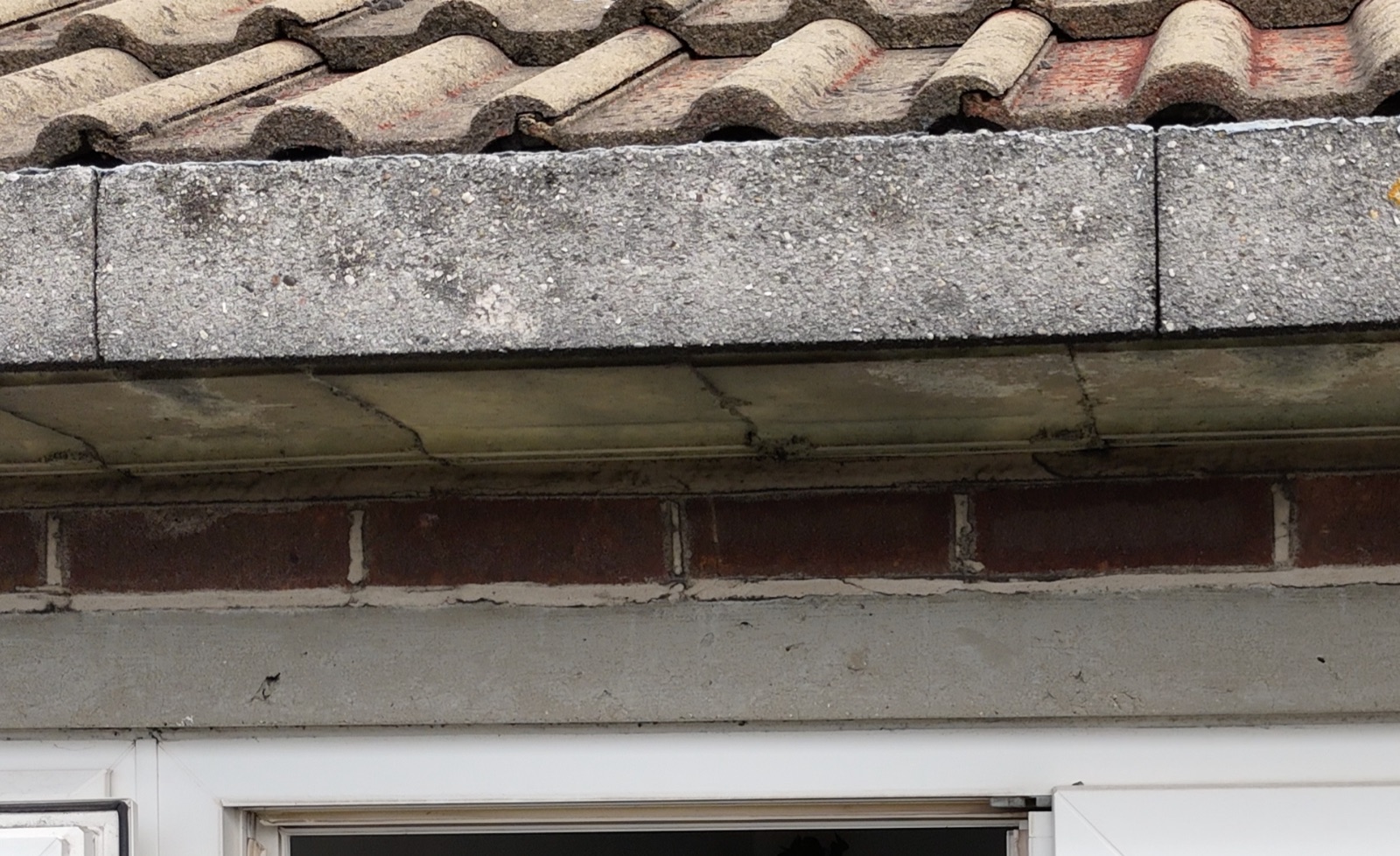 Elevation of a two-course precast concrete eaves gutter over a pair of glazed doors, showing the exposed aggregate trough unit, the smooth soffit blocks, a single brick course and the concrete lintel beneath.